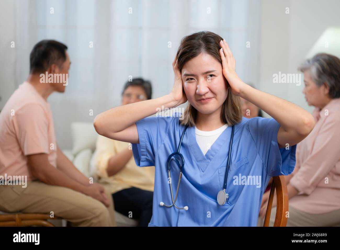 Young female nurse had to cover her ears with both hands. Due to the stress of the group of elderly people talking loudly. Healt Stock Photo