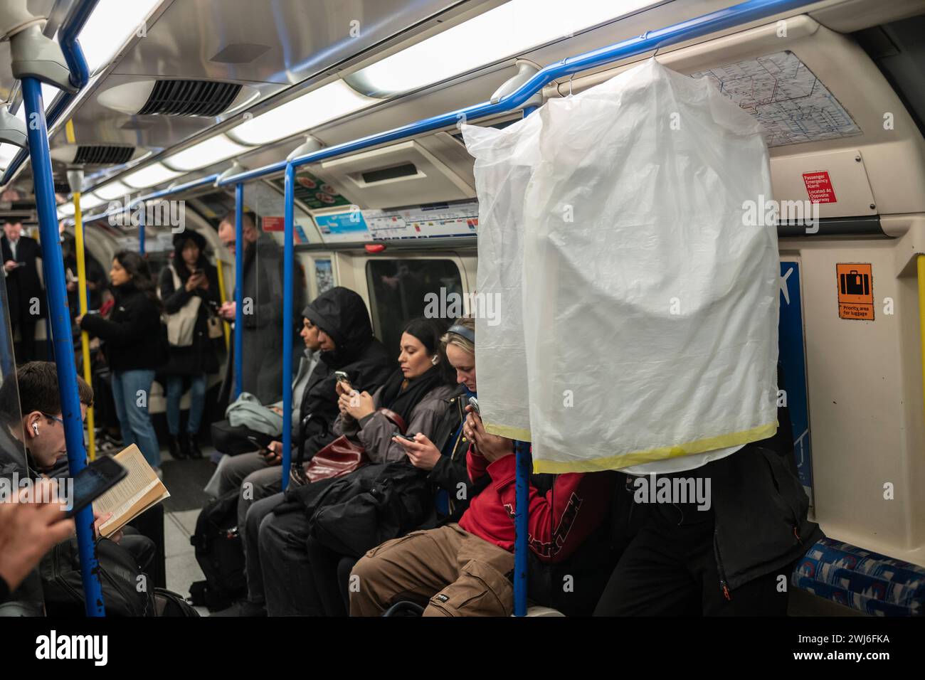 A commuter hangs their dry cleaning up inside the London Underground carriage as they travel into work, City of London, England, United Kingdom Stock Photo