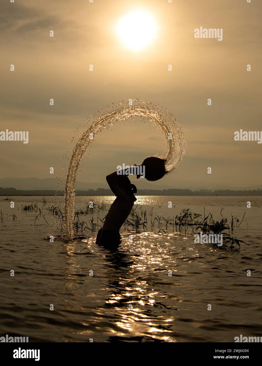 Silhouette of a fisherman in the water at sunset, Thailand. Stock Photo