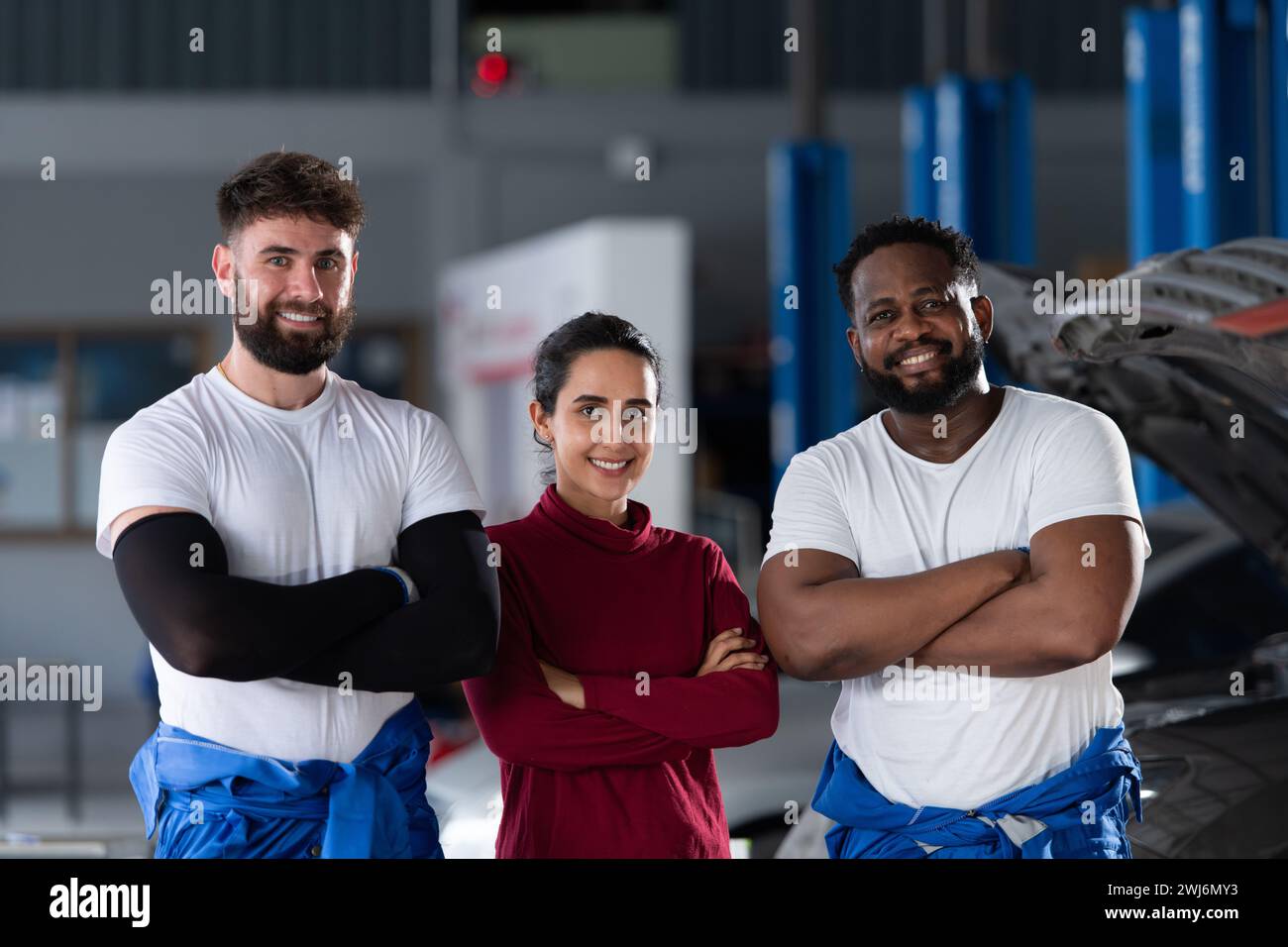 Portrait of two guy professional auto technician and a female customer standing in an auto repair shop with arms crossed Stock Photo