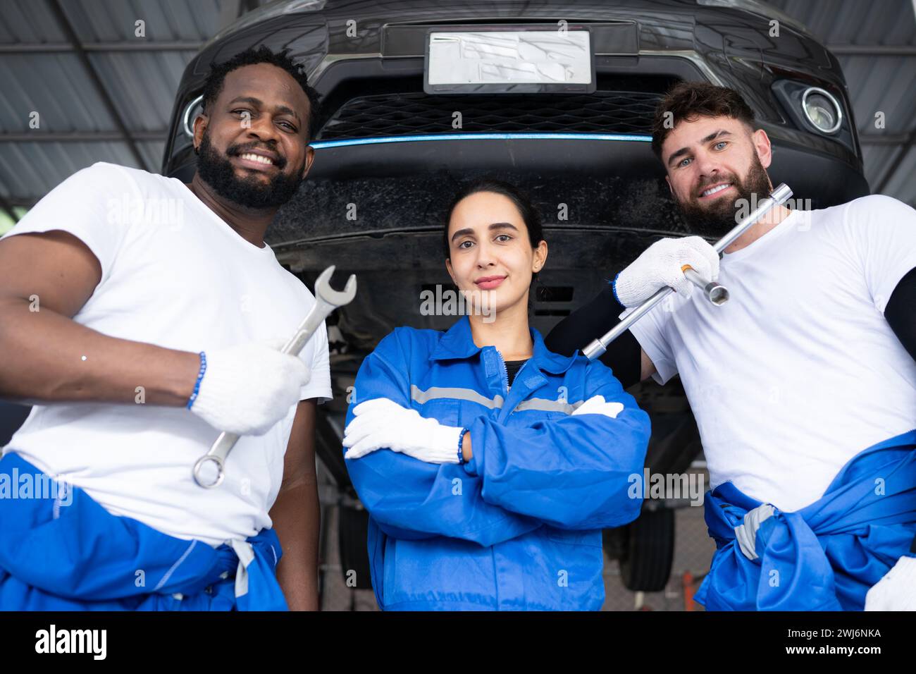 Portrait of smiling team of mechanics looking at camera while standing under car Stock Photo