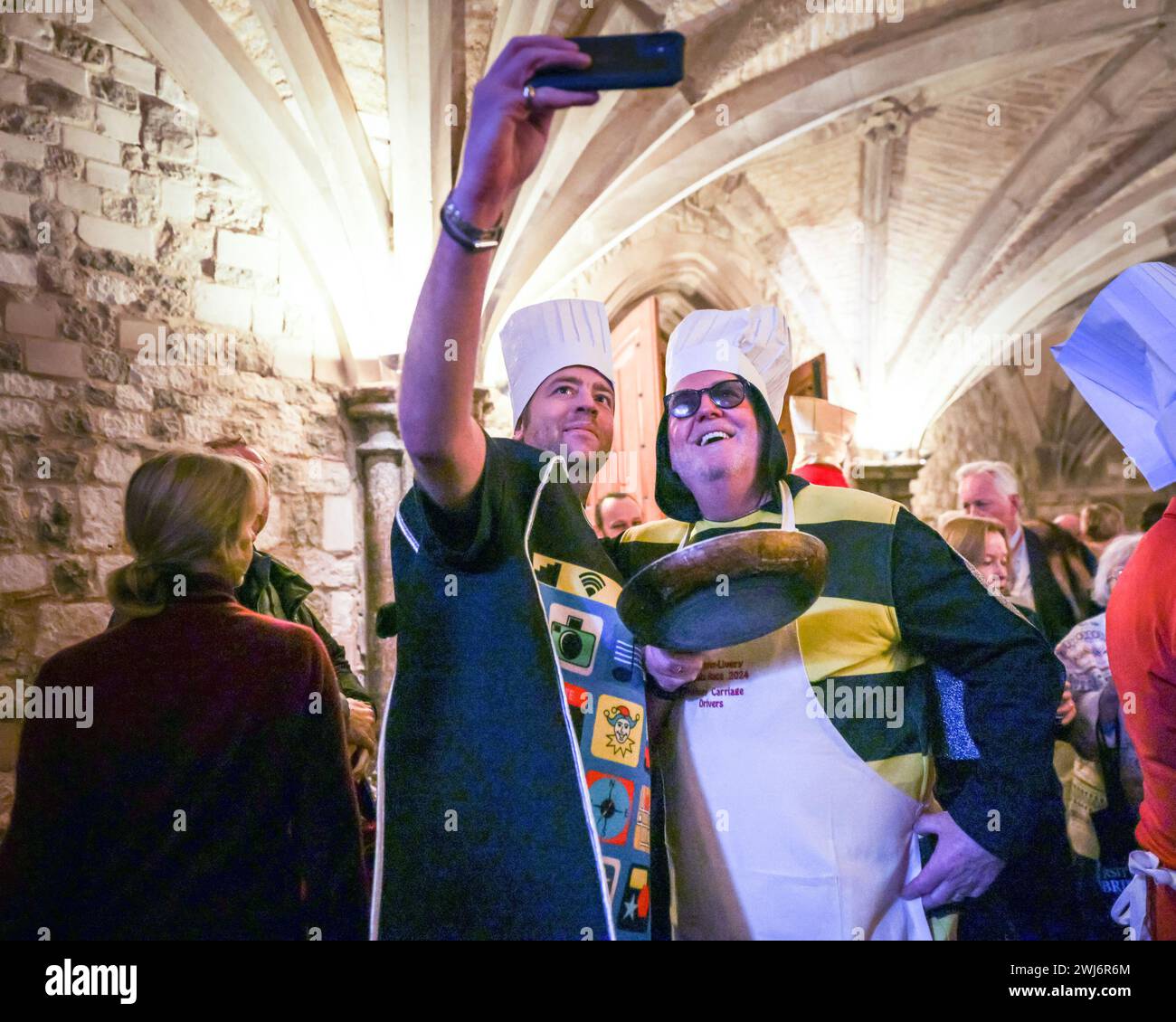 London, UK, 13th Feb 2024. Participants flee the rain into the Guildhall for food and judging of the costumes competition, which moved indoors. The annual Inter Livery Pancake Race normally sees teams of Livery Members from the City of London Worshipful Companies competing in Shrove Tuesday fun pancake races at Guildhall Yard, wearing either fancy dress or full regalia. Due to continued rain, the actual races had to be cancelled at short notice, but participants and judges enjoy a photocall 'toss up' before they move into the Guildhall for food and the judging of costumes. Stock Photo