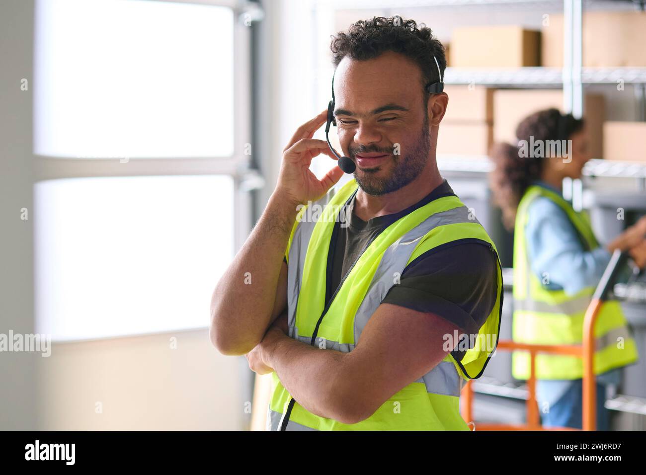 Man With Down Syndrome Working In Warehouse Wearing Headset Stock Photo