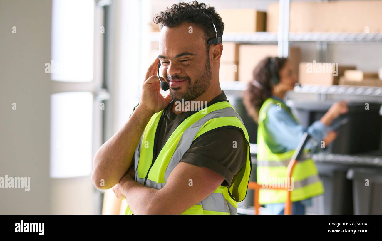 Man With Down Syndrome Working In Warehouse Wearing Headset Stock Photo