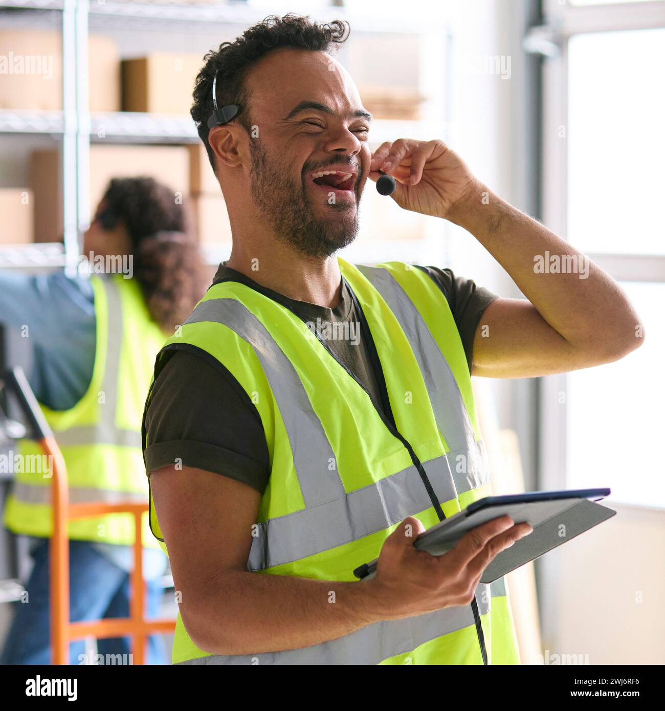 Man With Down Syndrome Working In Warehouse Wearing Headset Using Digital Tablet Stock Photo