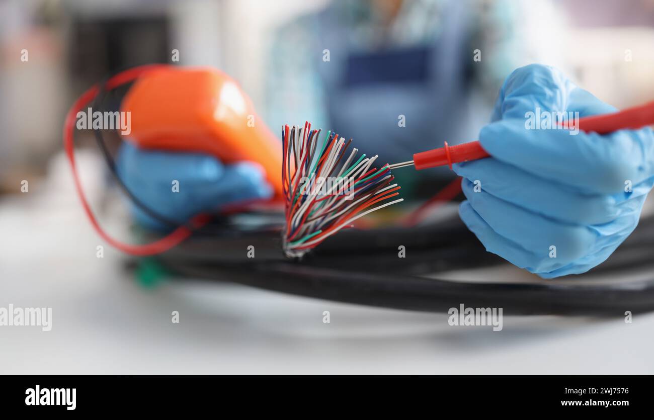 Hands with a voltmeter check colored wires in the cable, blurry Stock Photo