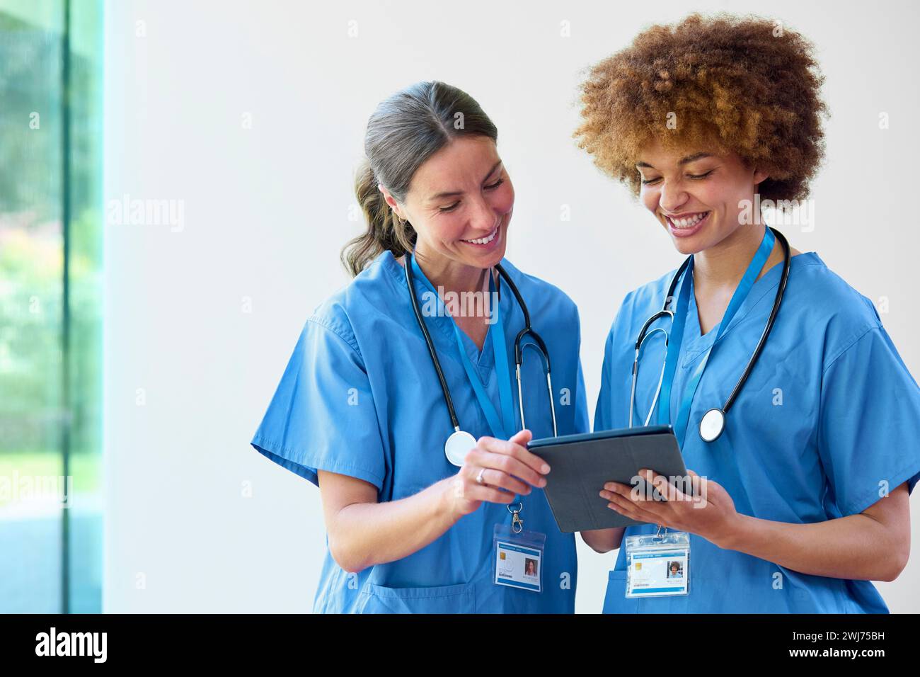 Two Female Doctors Wearing Scrubs With Digital Tablet Discussing Patient Notes In Hospital Stock Photo
