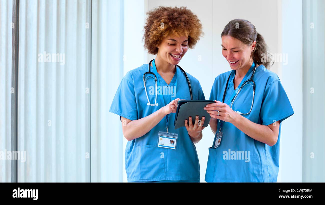 Two Female Doctors Wearing Scrubs With Digital Tablet Discussing Patient Notes In Hospital Stock Photo