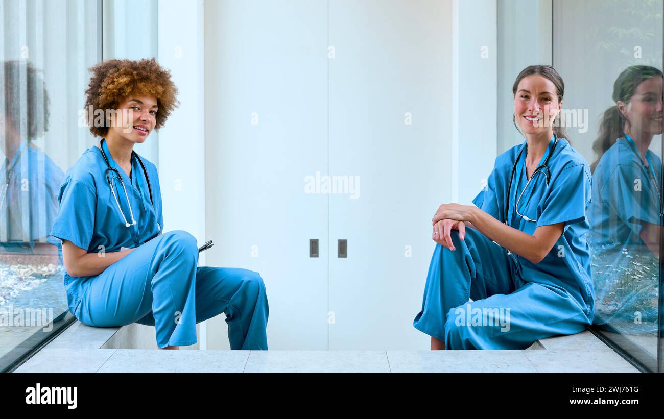 Portrait Of Two Female Doctors Wearing Scrubs Taking A Break In Modern Hospital Stock Photo