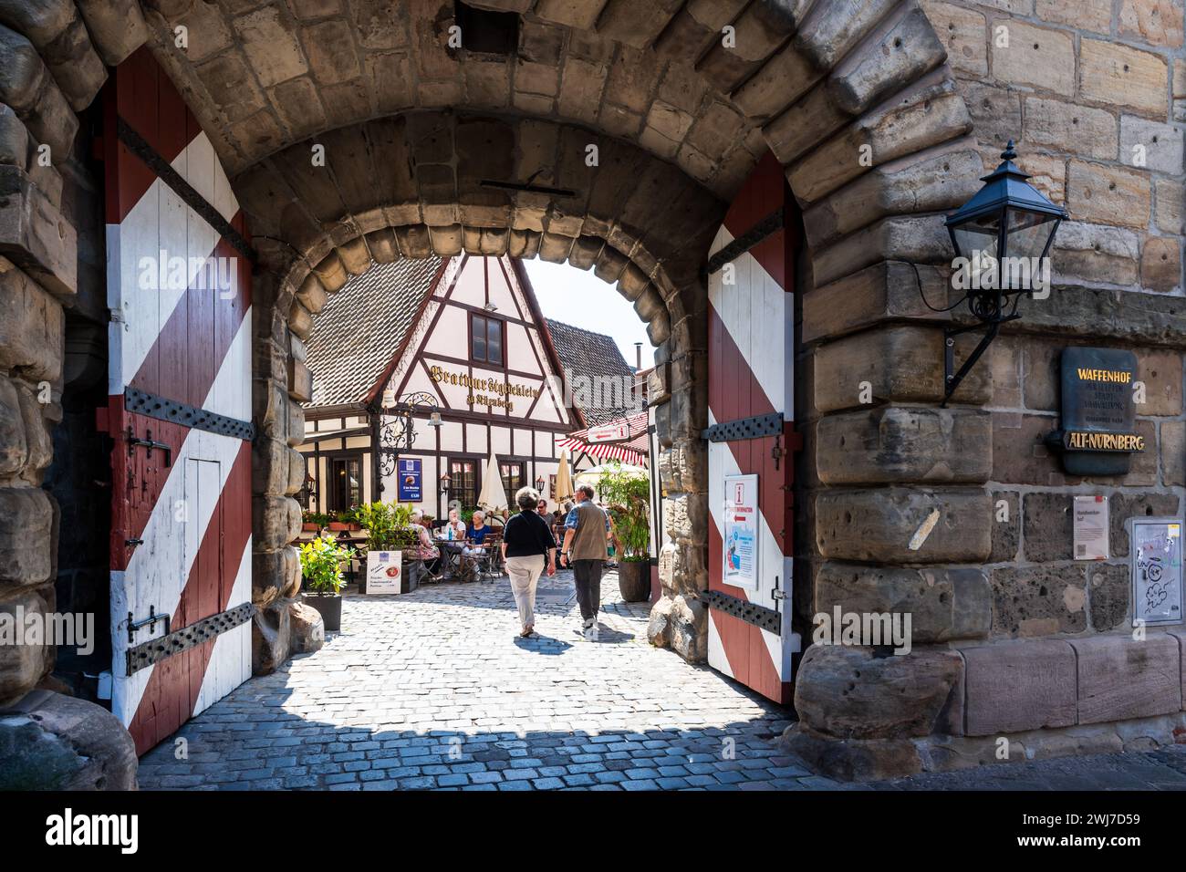 Senior tourists walk through the gate of the Handwerkerhof in Nuremberg, Germany, a craftmen's yard in the old town with craft shops and restaurants. Stock Photo