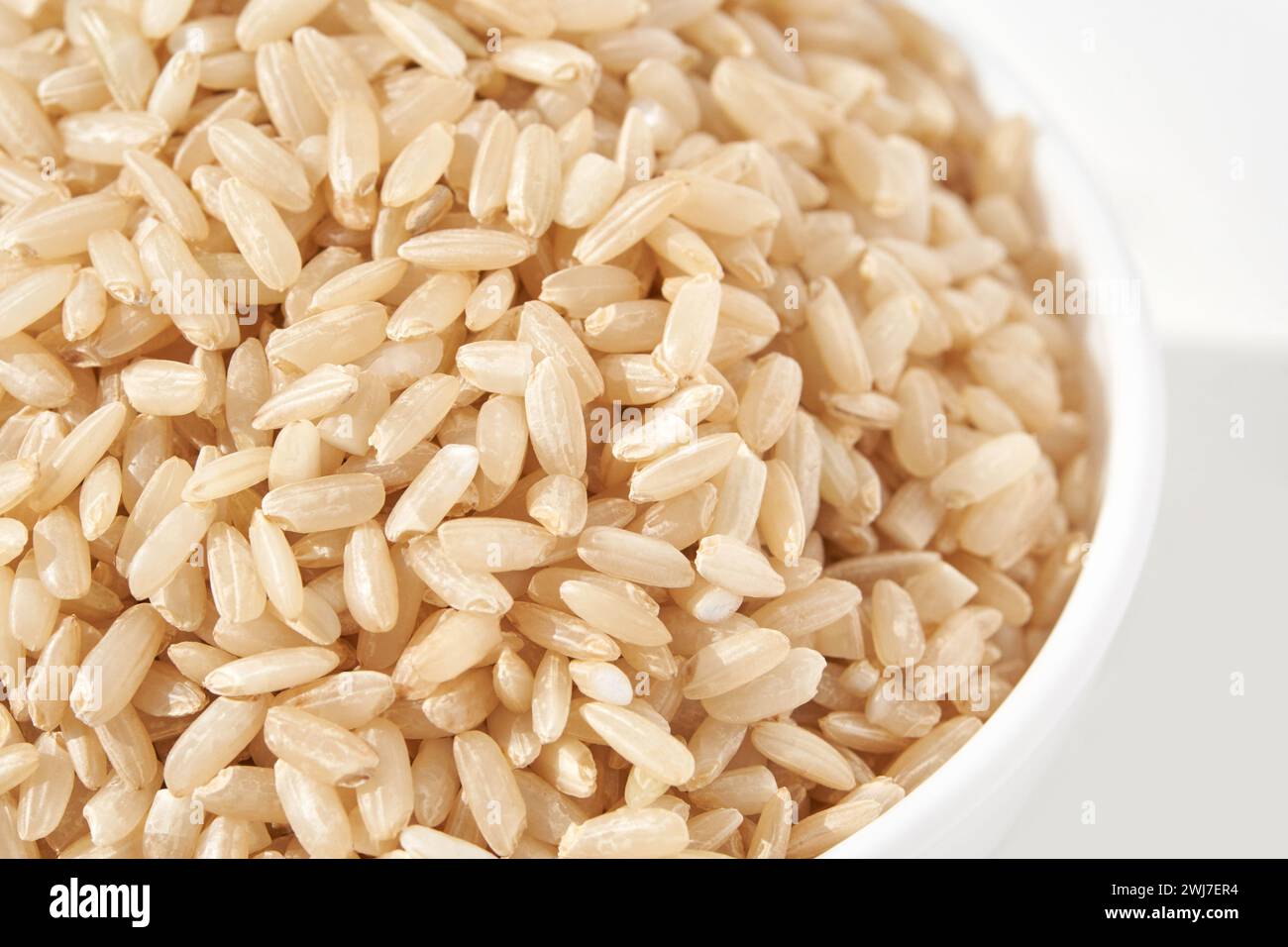 A bowl of uncooked brown rice, isolated against a white background