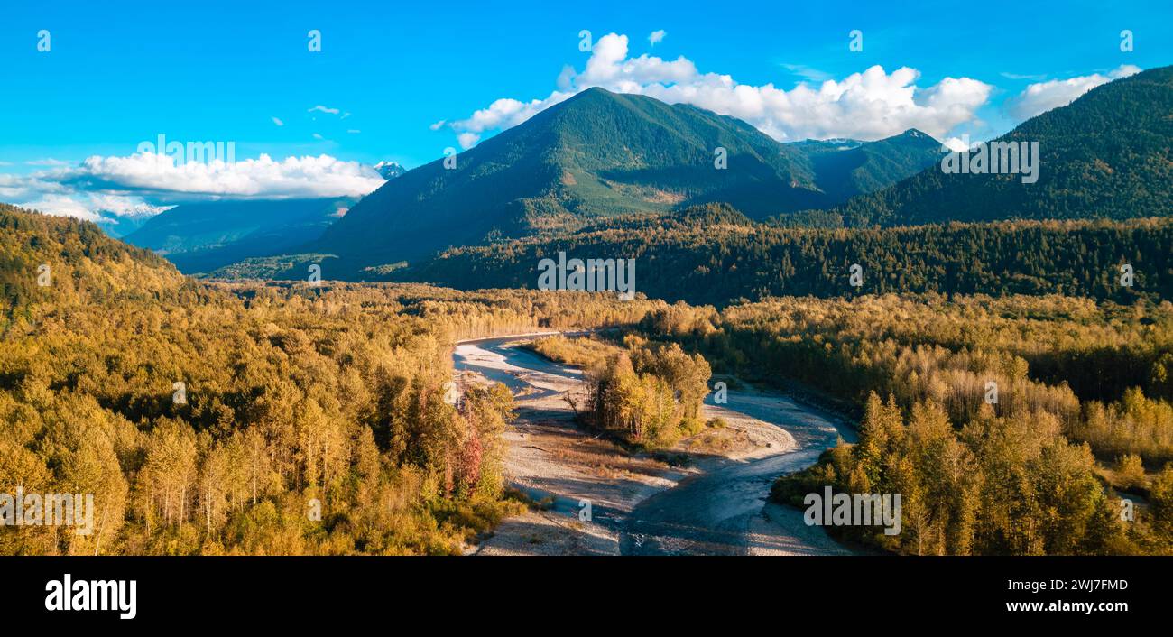 Mountain scene with river, lush forests, and majestic peaks in the backdrop Stock Photo