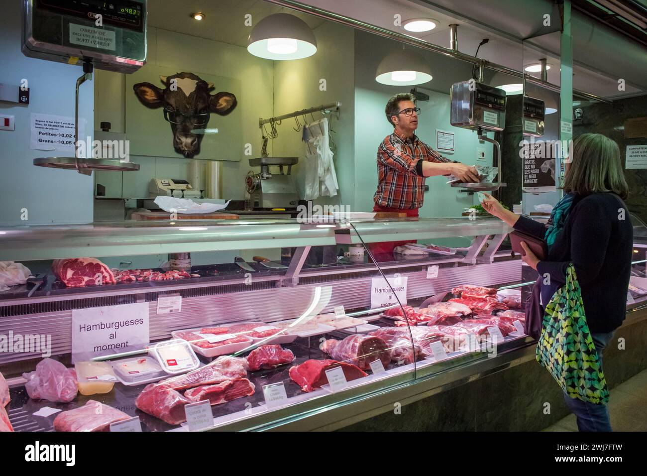 Butcher weighing meat for a customer in the old Abaceria Central Market, Barcelona Stock Photo