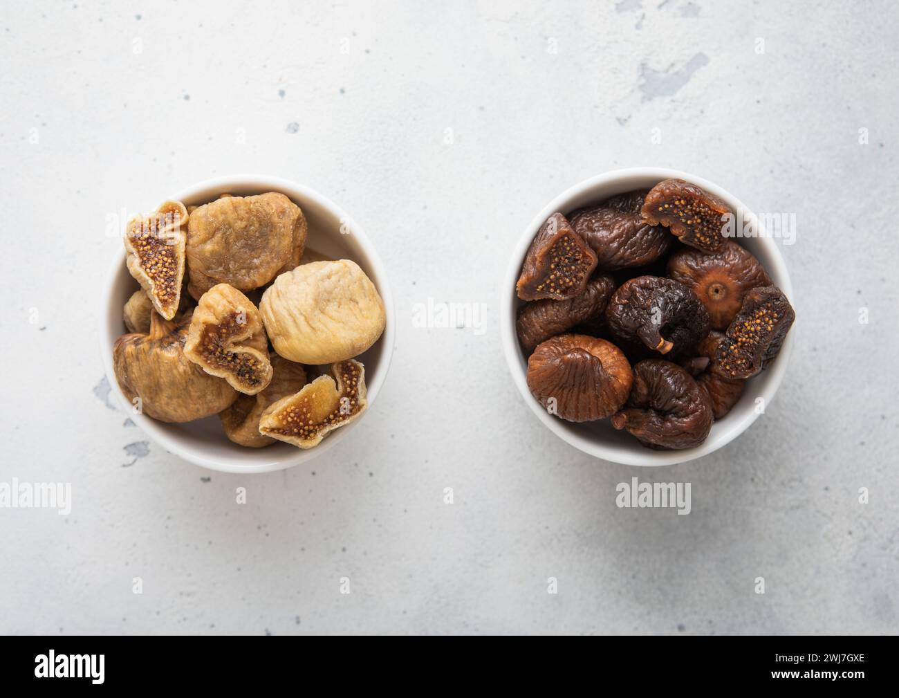 Two kitchen bowl plates with white and brown organic dried organic figs on light background. Stock Photo