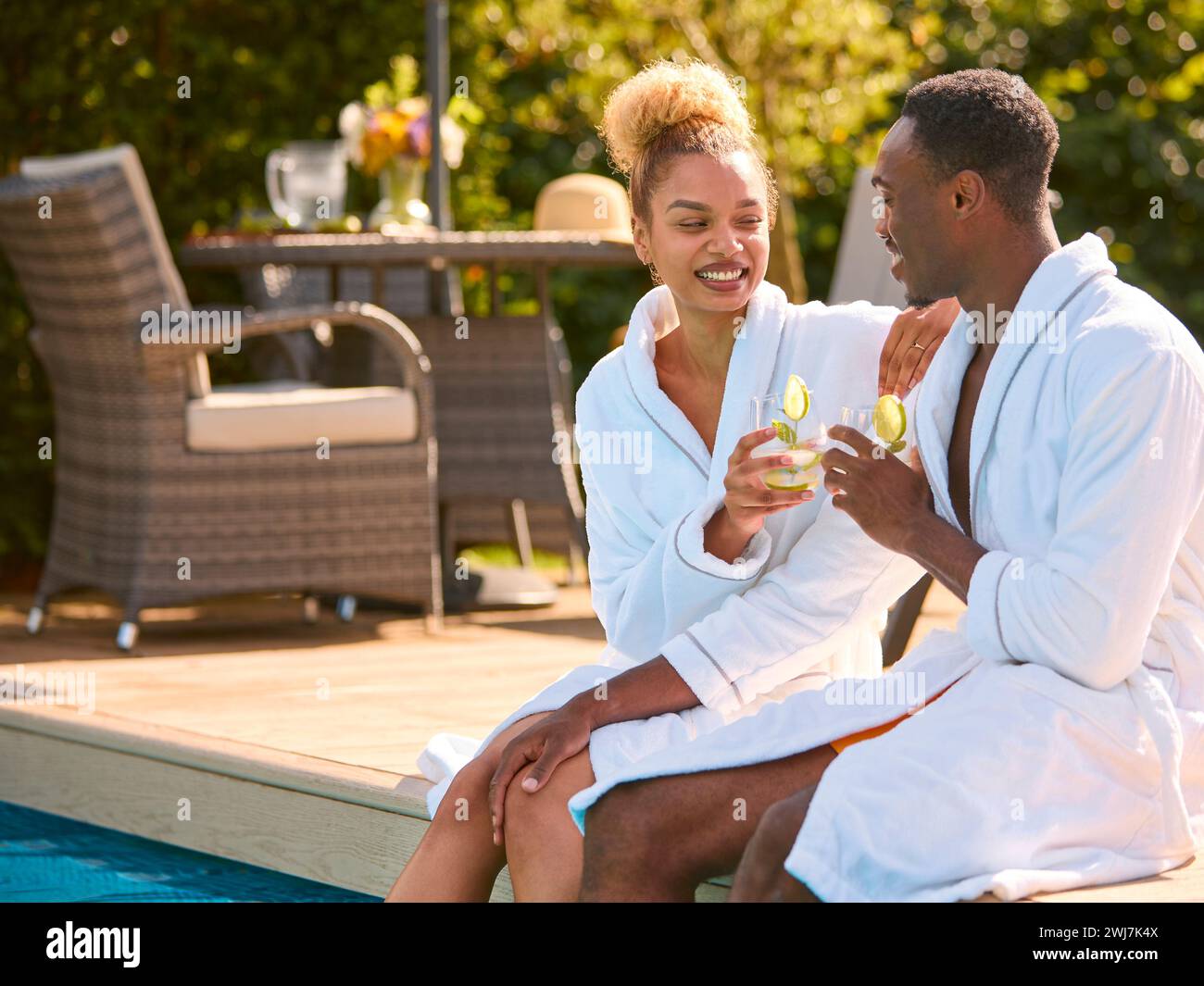 Couple Wearing Robes Outdoors Sitting With Drinks With Feet In Swimming ...
