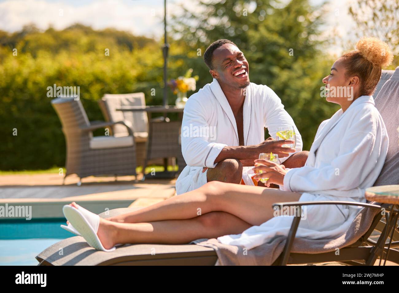 Couple Wearing Robes Outdoors Sitting With Drinks On Loungers Around ...