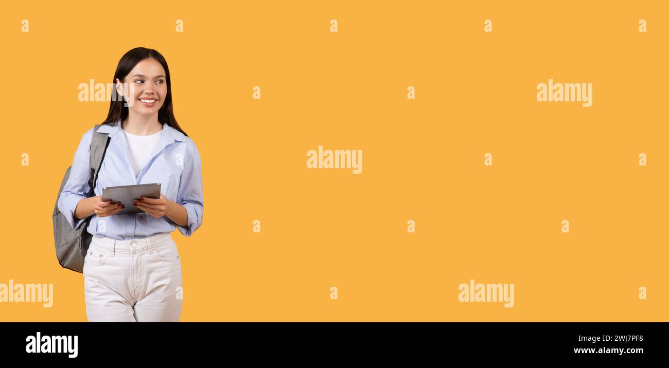 Smiling lady student using digital tablet with standing with backpack, looking at free space Stock Photo