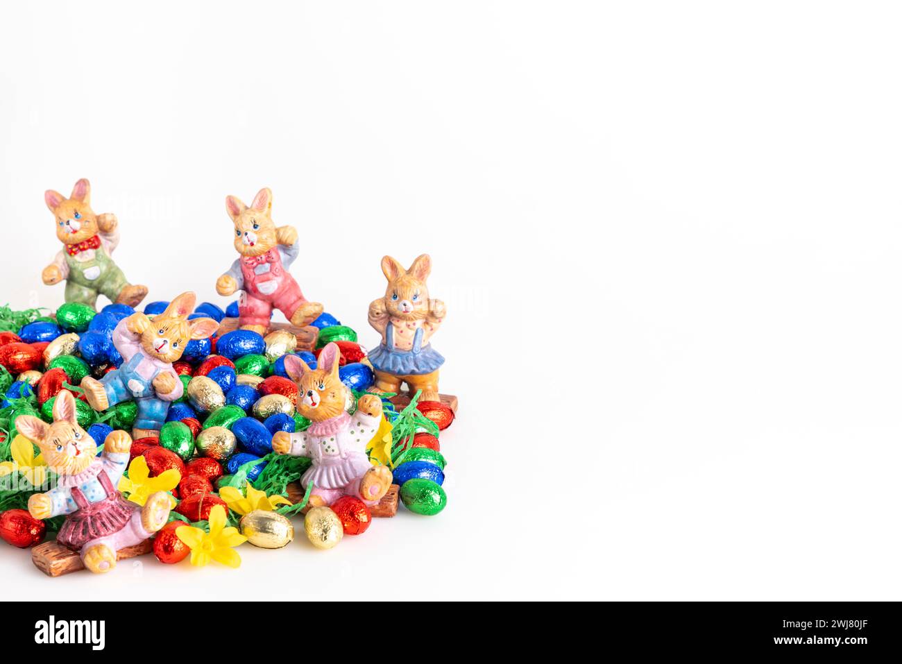 Several Easter bunny figures surrounded by colourful chocolate eggs on artificial grass, white background Stock Photo