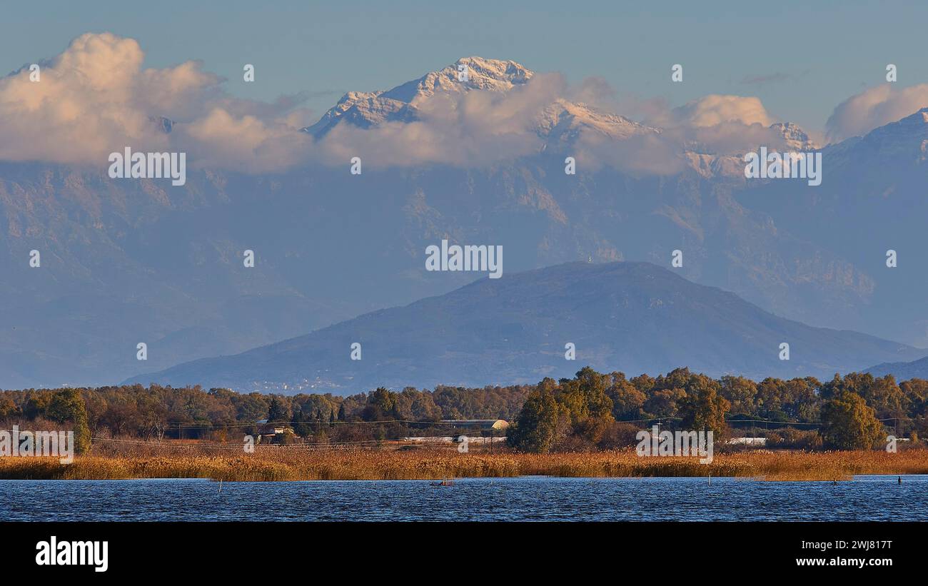 Snow-capped mountain peaks rise behind a landscape with water ...