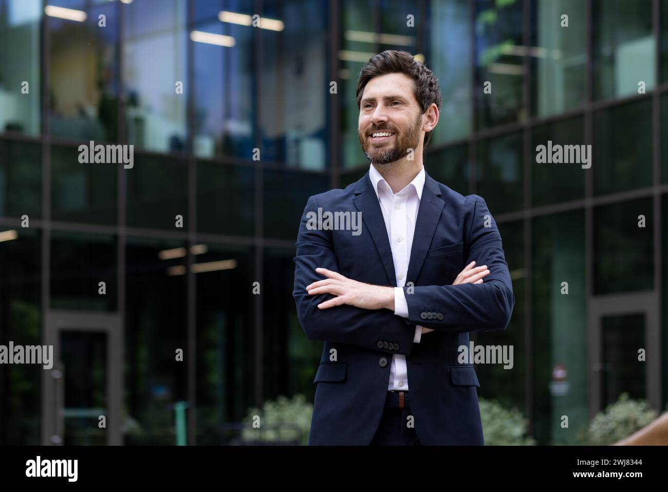 Smiling mature businessman in a suit standing confidently outside a contemporary office building, exuding leadership. Stock Photo
