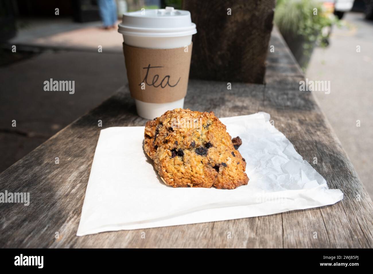 Homemade scone and tea in a paper cup outside on a bench Stock Photo