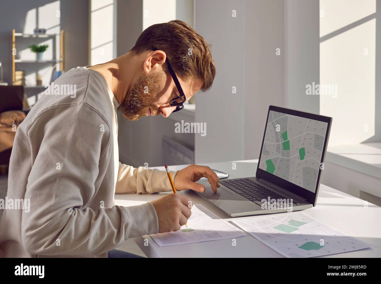 Professional cartographer working with printed cadastral map at table on his workplace. Stock Photo