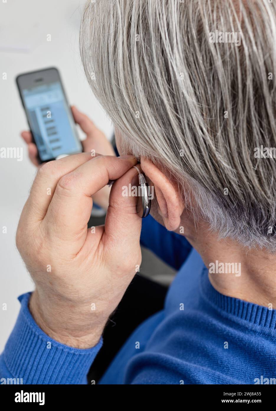 Elderly man with hearing loss with behindtheear hearing aid adjusting