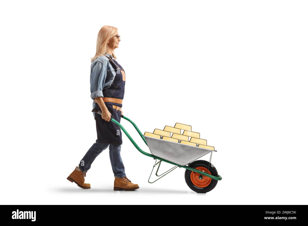 Full length profile shot of a female gardener pushing a wheelbarrow with gold isolated on white background Stock Photo