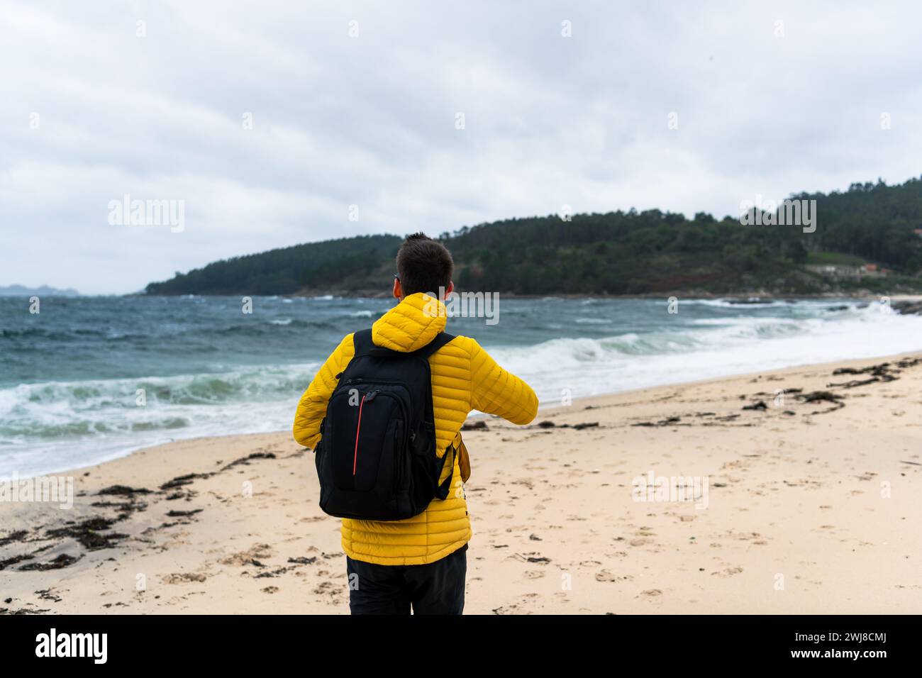 Man walking on a white sand beach with a yellow jacket Stock Photo - Alamy