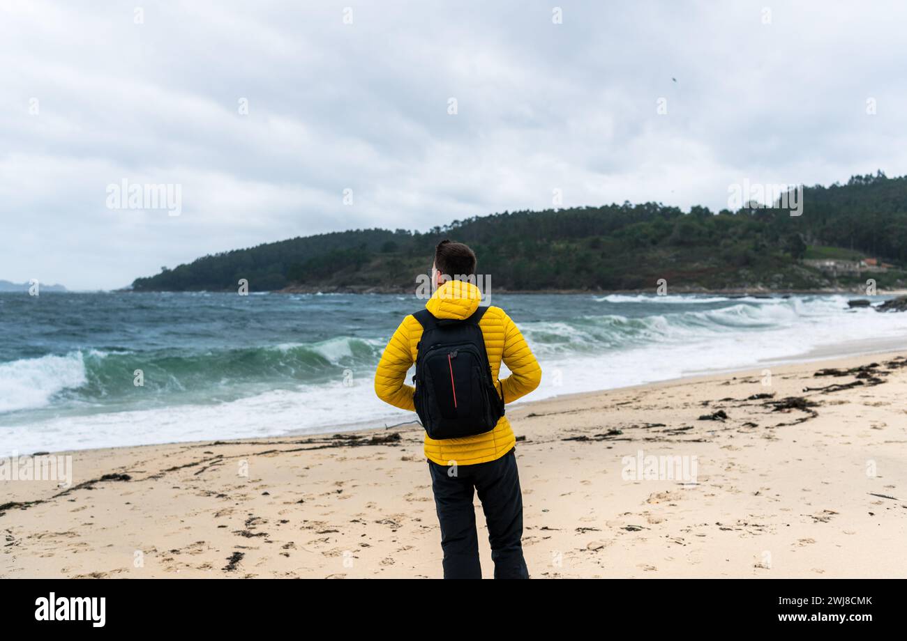 Man walking on a white sand beach with a yellow jacket Stock Photo - Alamy