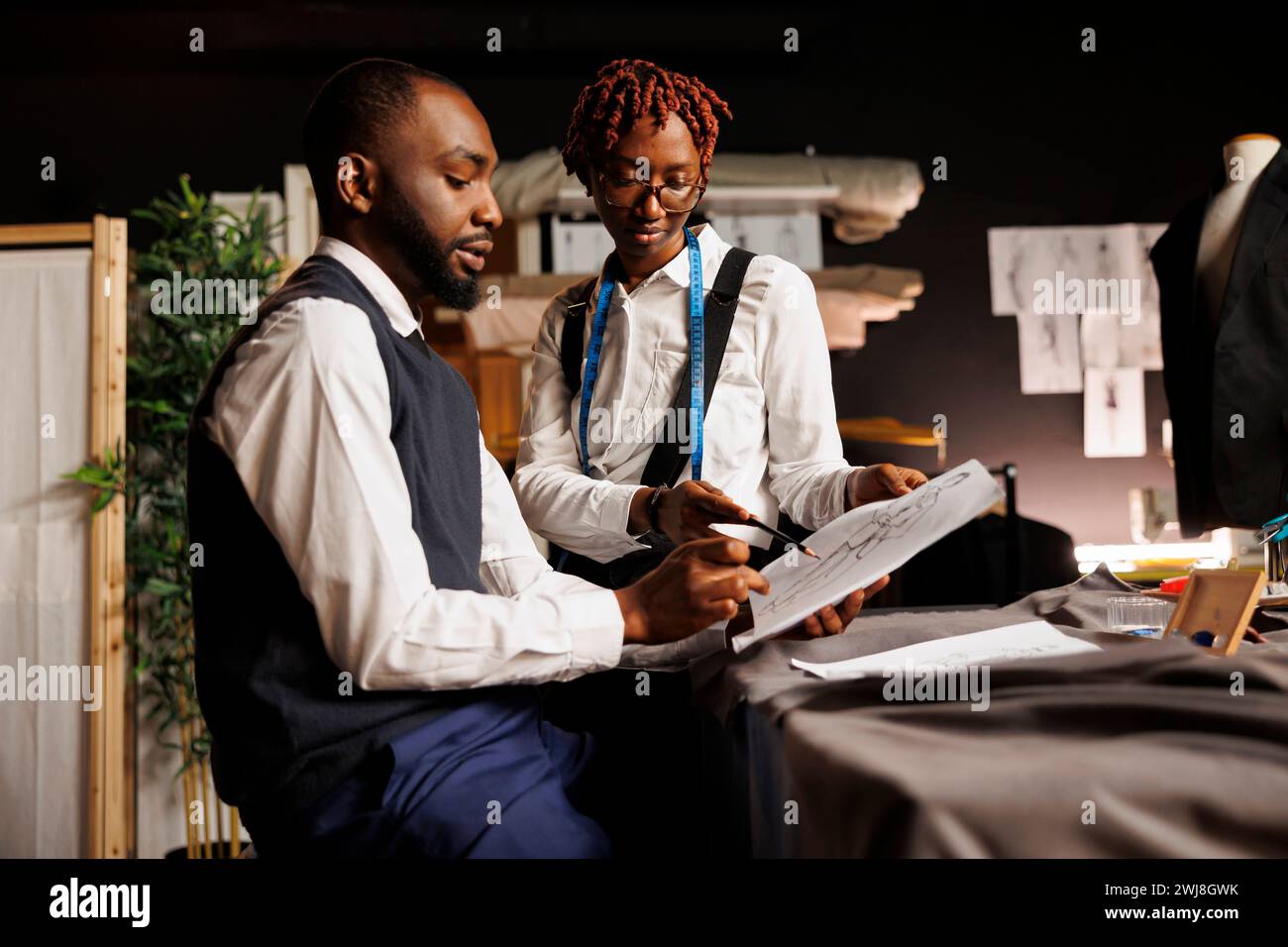 Brainstorming apprentice tailors looking over sketch drawings of ...