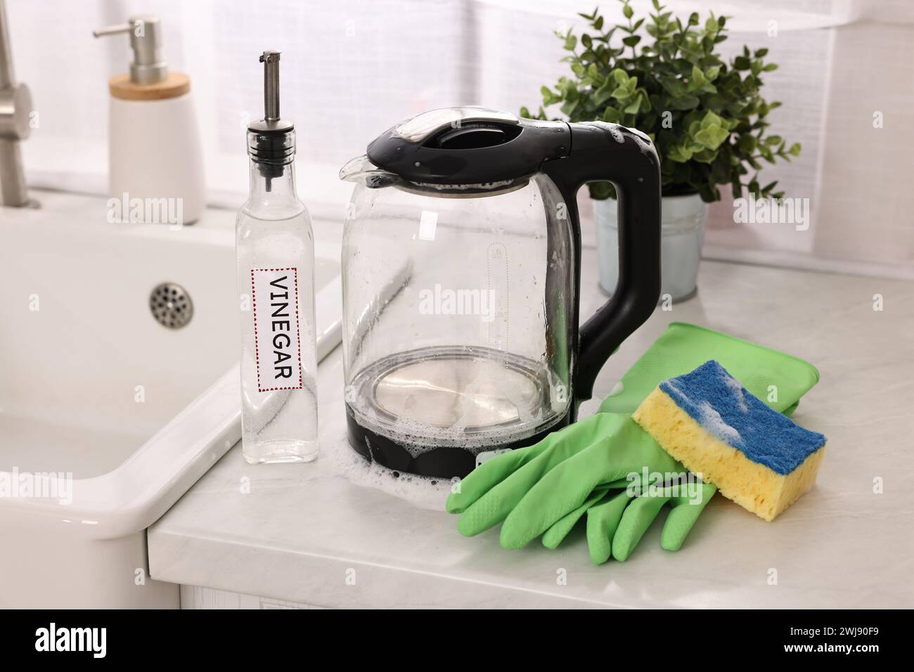Cleaning electric kettle. Bottle of vinegar, rubber gloves and sponge with foam on countertop in