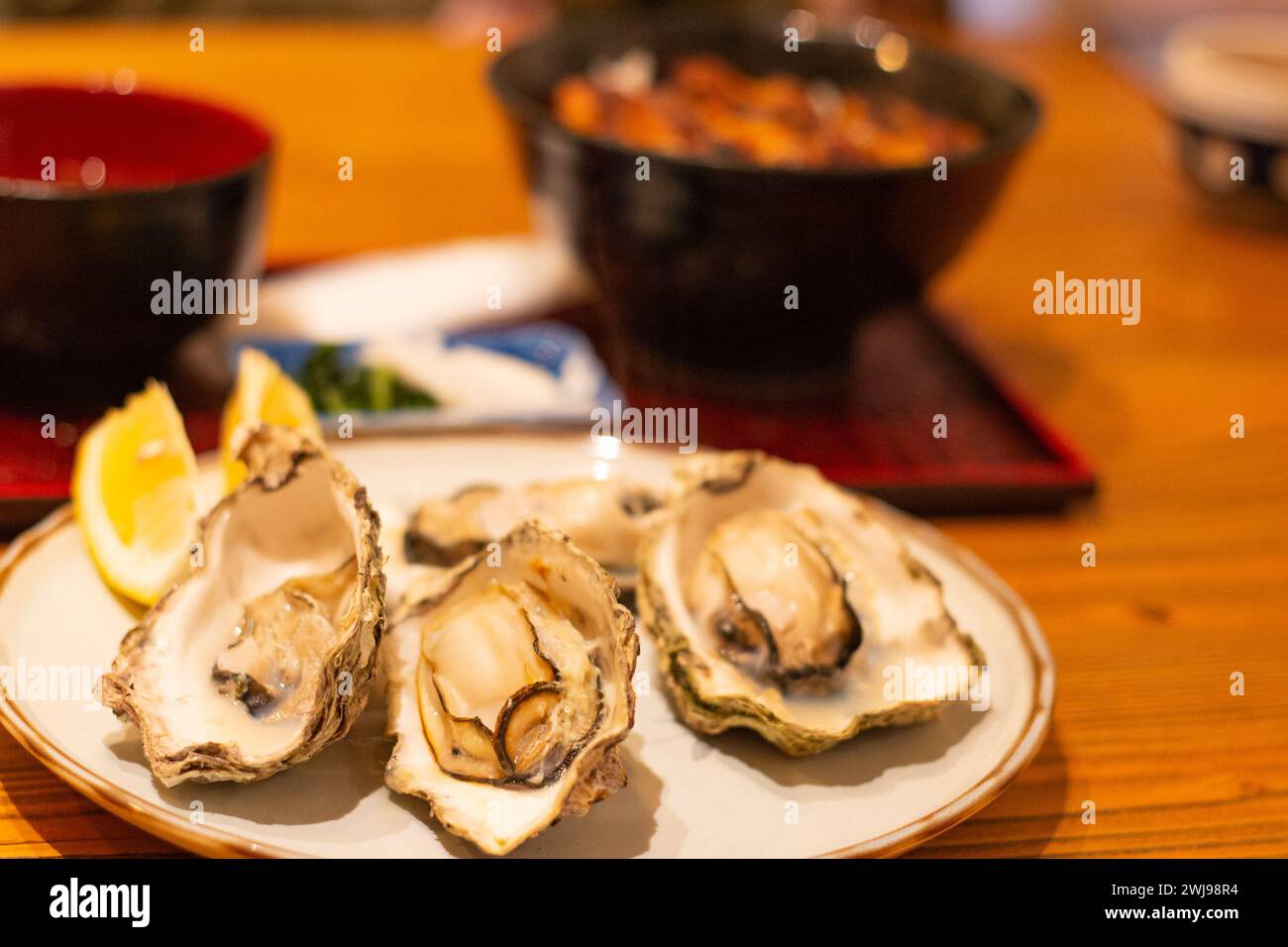 Plate of dlicious grilled oysters served with slices of lemon on table, Hiroshima, Japan, soft focus, selective focus on the front oyster Stock Photo