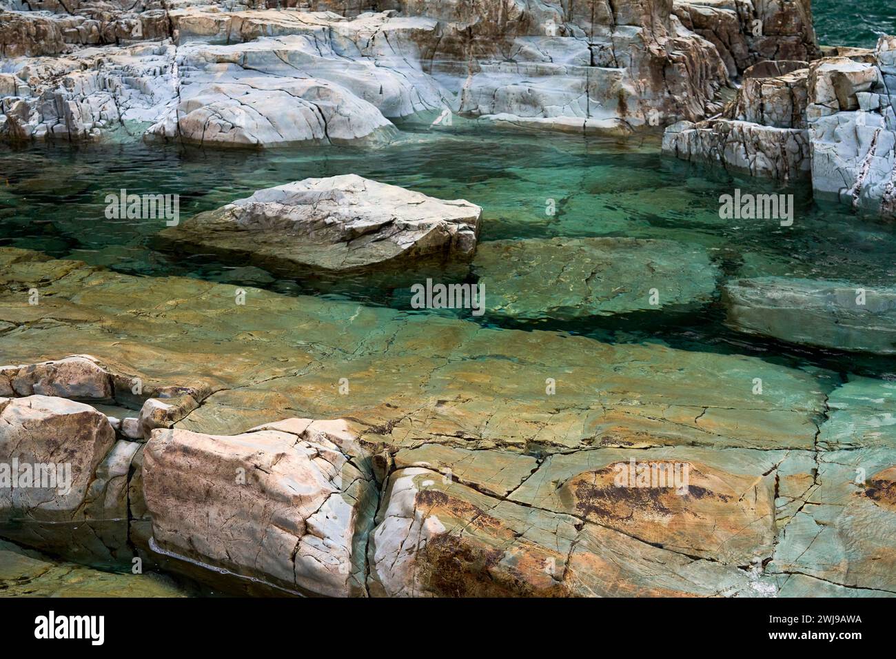 Transulcent brilliant aqua water following over the colorful boulders and rocks at a wilderness park Stock Photo