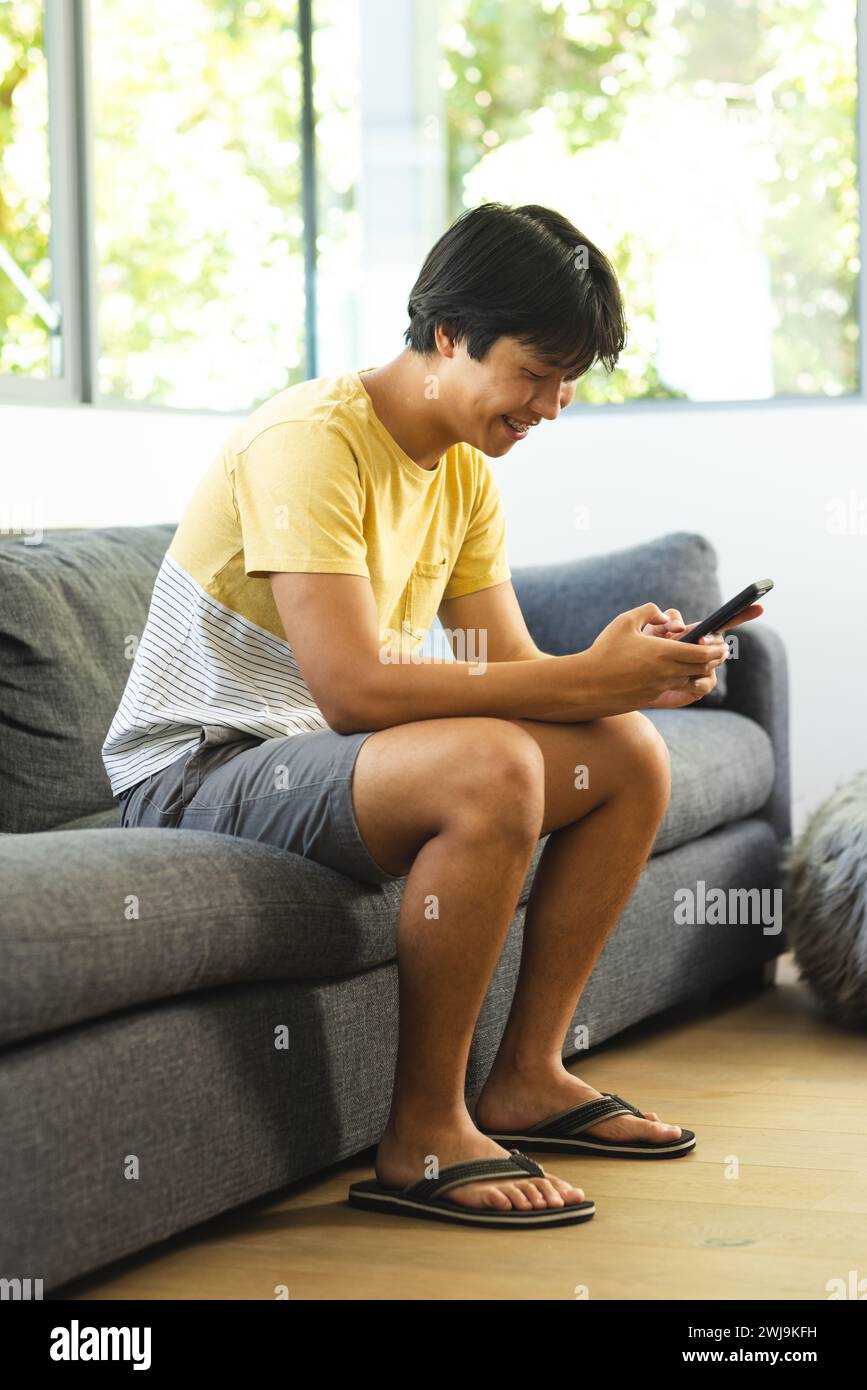 Teenage Asian boy sits on a couch at home, engrossed in his smartphone Stock Photo