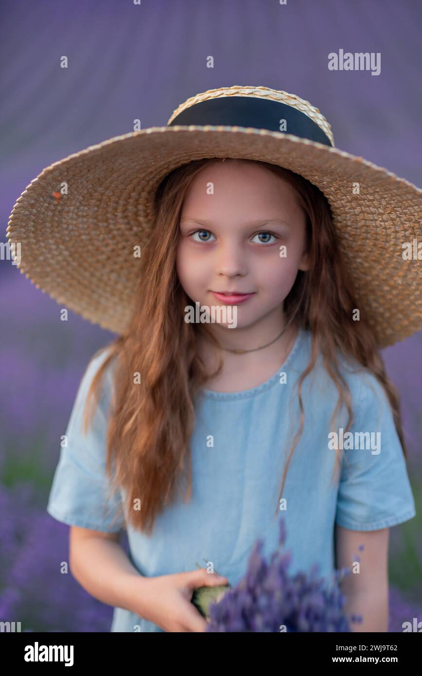 Girl lavender field in a blue dress with flowing hair in a hat stands ...