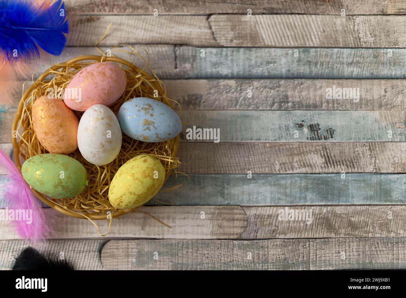 Flat lay composition of colourful painted easter eggs in a hay basket on wooden table. Happy Easter celebration Stock Photo