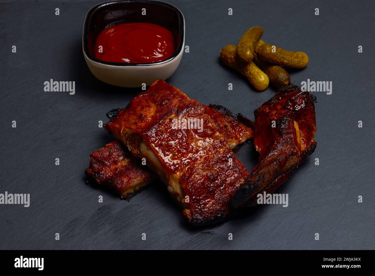 pork ribs with sauce and pickled cucumbers on a stone plate ready to be ...
