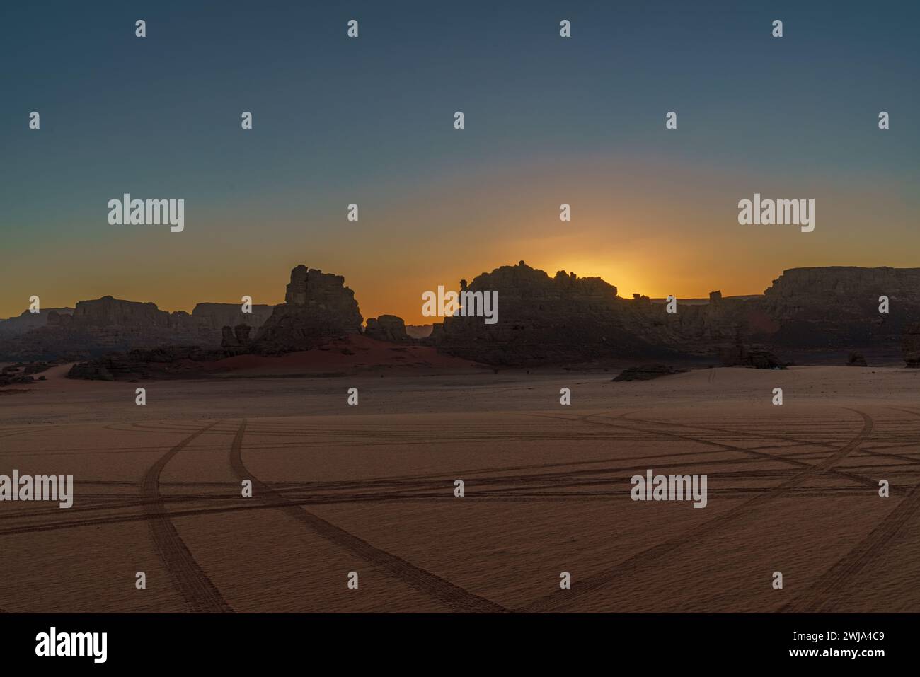 A serene sunset casts a warm glow over the rugged terrain of Tadrart ...