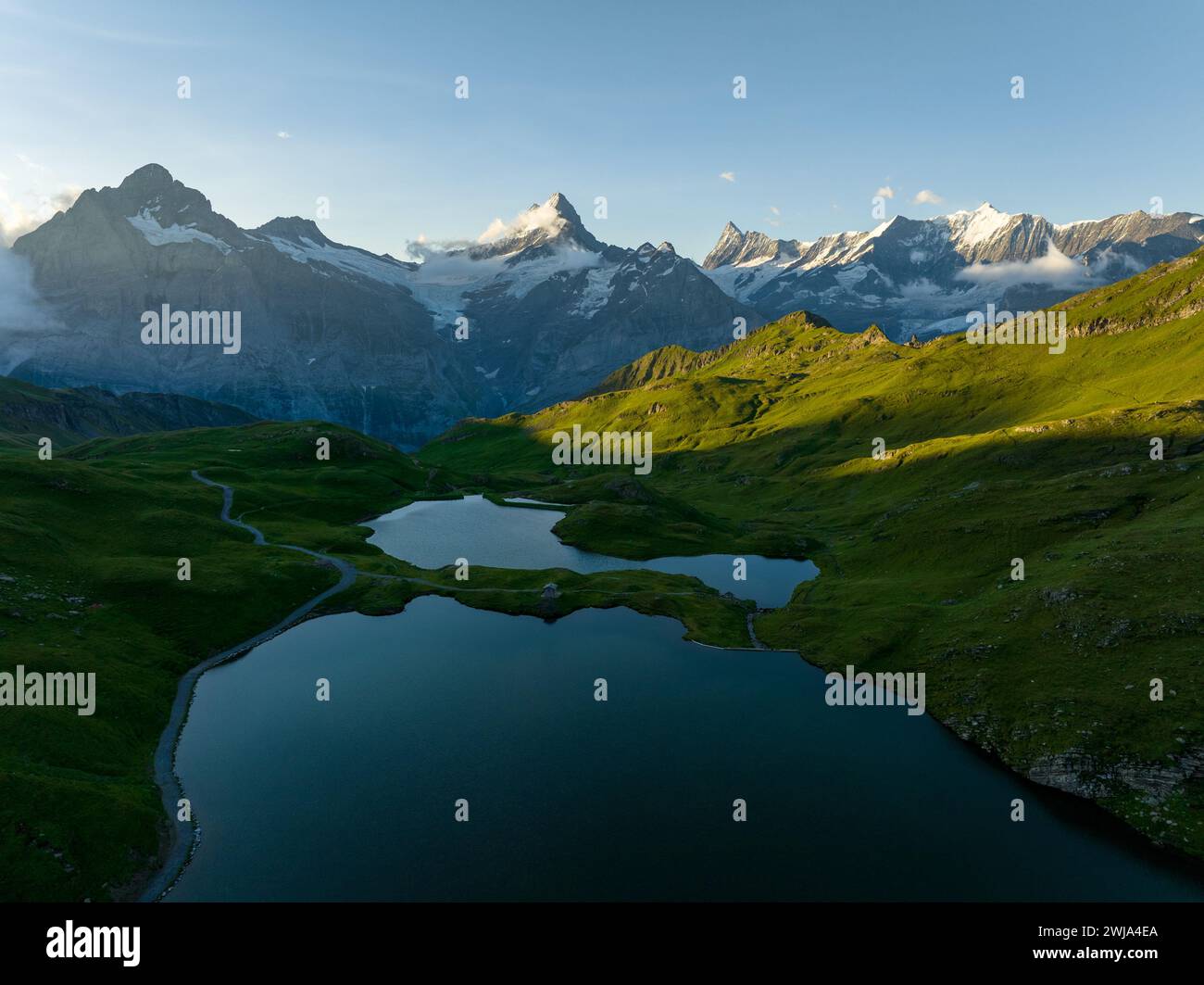 A tranquil evening view of Bachalpsee Lake surrounded by the lush greenery with the Swiss Alps in the background, bathed in the warm light of the sett Stock Photo