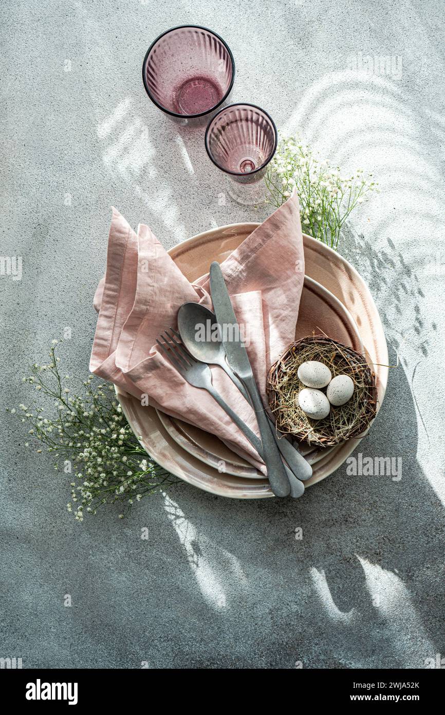 Top view elegant and simple table setting celebrates Easter with a bird's nest containing speckled eggs, surrounded by delicate china and soft pink li Stock Photo