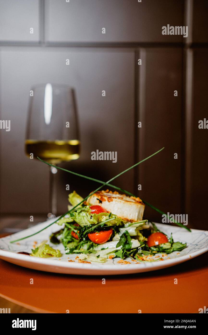 Elegant presentation of a gourmet salad with cherry tomatoes, served on a stylish plate with a glass of white wine in the background Stock Photo