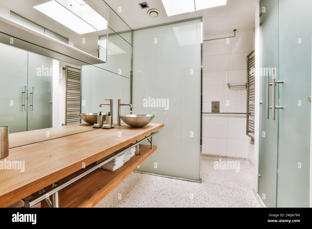 A sleek modern bathroom featuring wooden vanity, glass shower doors, and metallic fixtures illuminated by natural light. Stock Photo