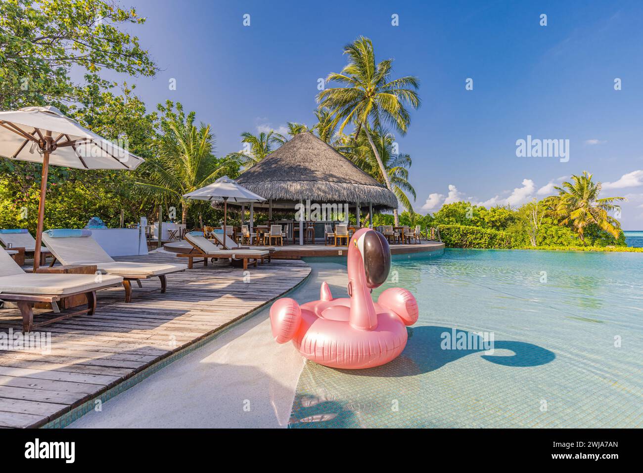 Summer tourism swimming pool inflatable pink flamingo, luxury resort hotel poolside. Happy cloudy sky, tropical paradise island infinity pool sea view Stock Photo