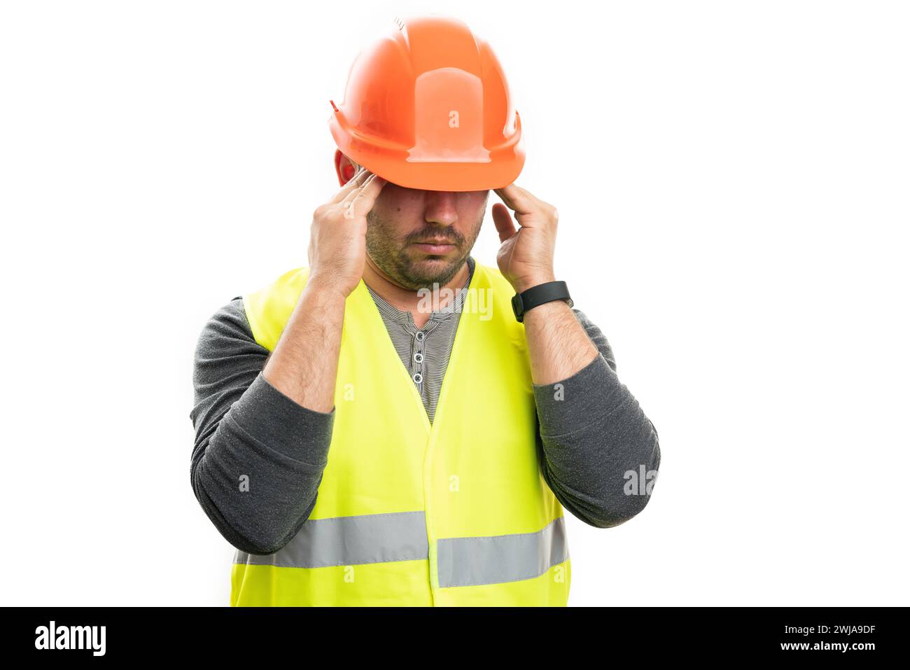 Male adult constructor touching temples as painful migraine as stressed concept wearing work attire safety orange helmet and fluorescent vest isolated Stock Photo