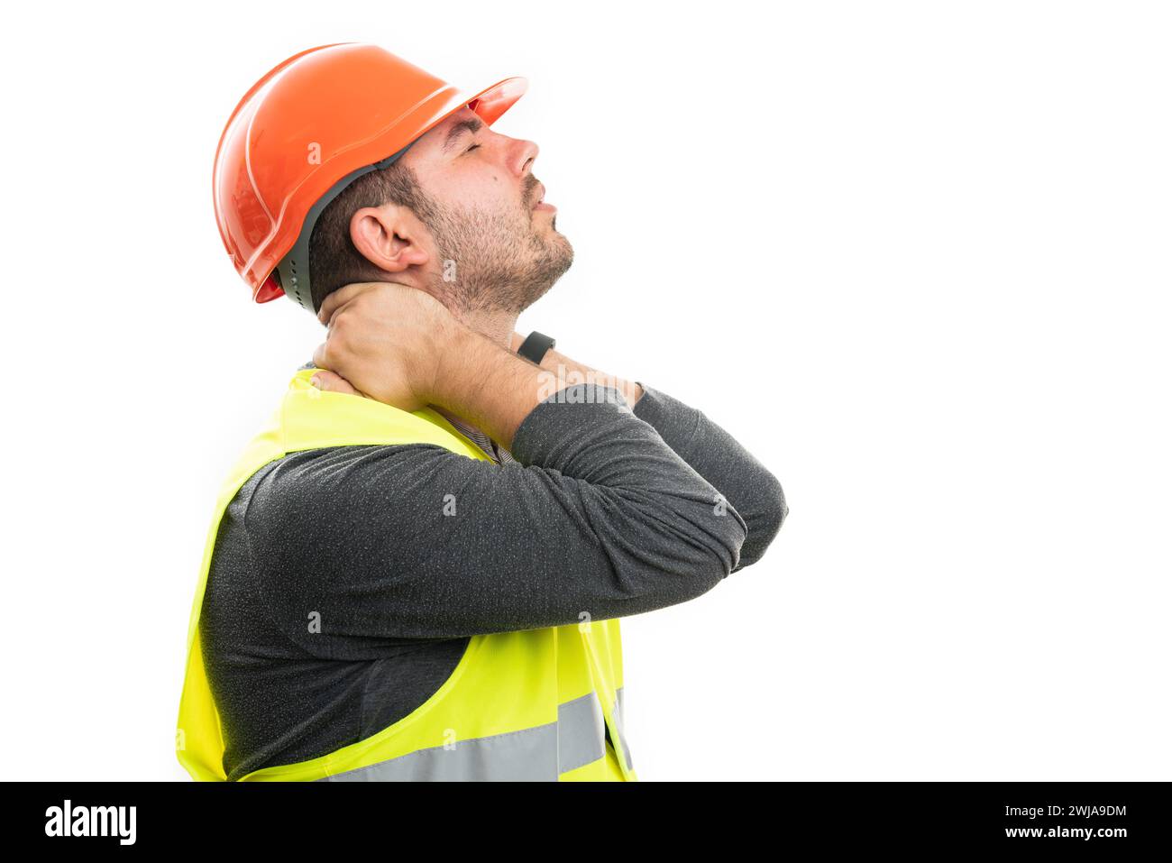 Male builder in pain touching hurting back of neck as muscle strain concept in work attire helmet and vest isolated on white studio background Stock Photo