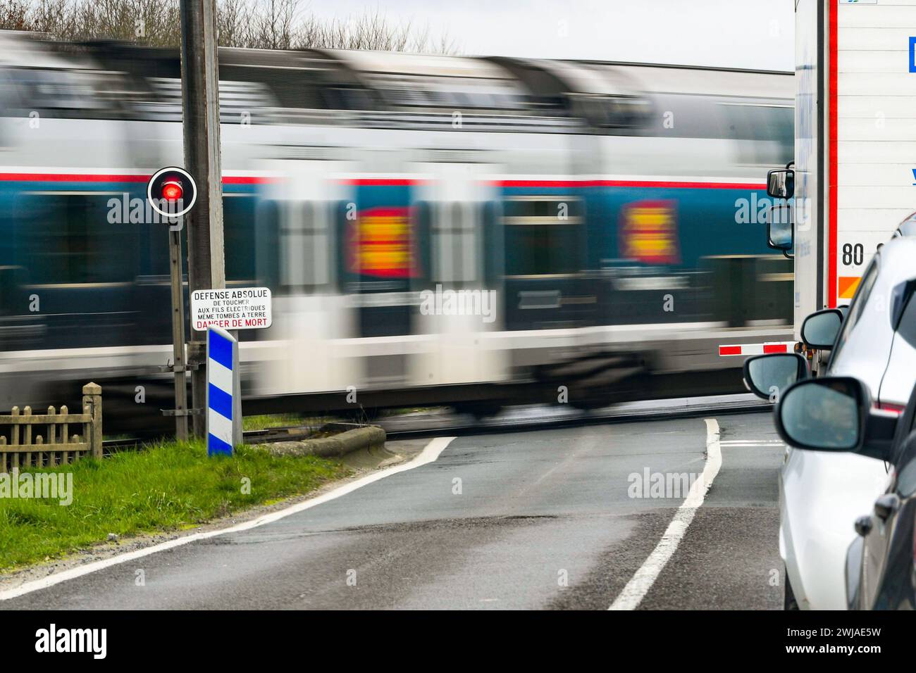 Railway level crossing on a country road with automatic railway gate. Automatic gates down, gates closed, red flashing light and cars at a standstill Stock Photo