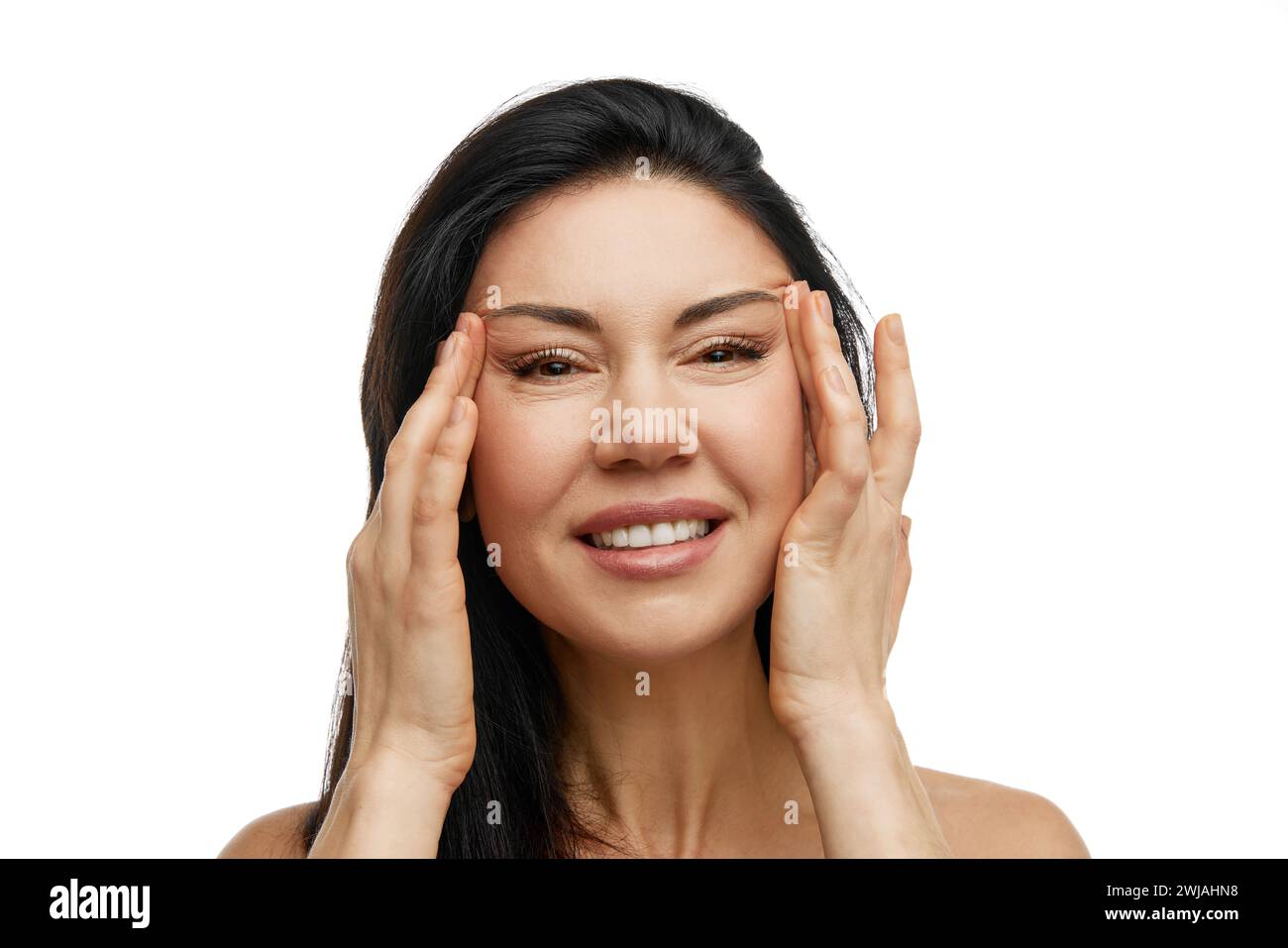 Close up portrait of smiling middle aged woman with hands on temples ...