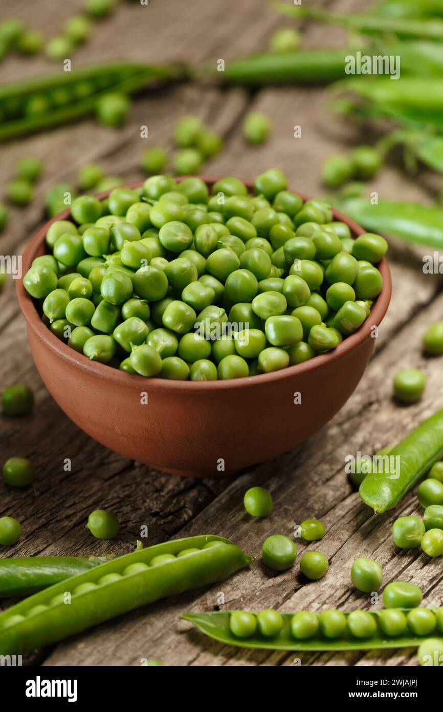 Fresh organic green peas in closed and open pods, scattered pea seeds, shelled green peas in a clay bowl on an aged wooden background. vegetable prote Stock Photo