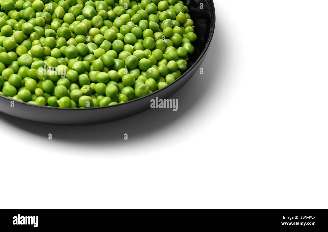 Peeled grains of fresh green peas in a round black plate on a white background, copy space. Vegetable protein, healthy products. Stock Photo